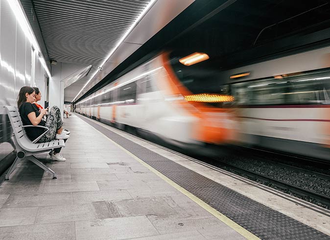2 people sitting on a bench inside a metro station with a metro driving past