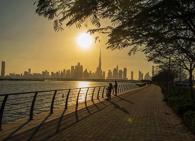 the sun setting over the skyline of Dubai with two people in the foreground fishing