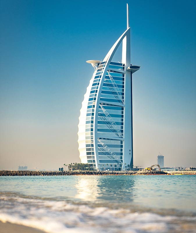 a famous tall building in Dubai shaped like a sail, with the beach in the foreground