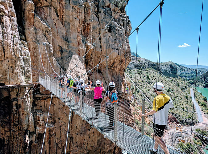several people walking across a metal bridge over a cliff