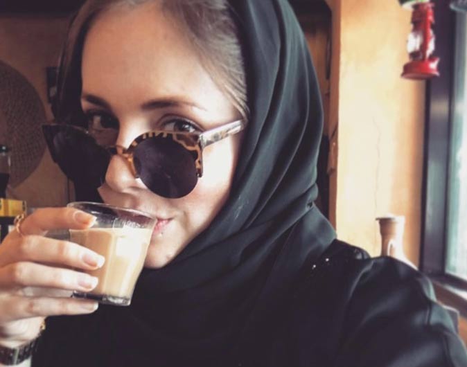 a woman with a black scarf and sunglasses sipping milky tea