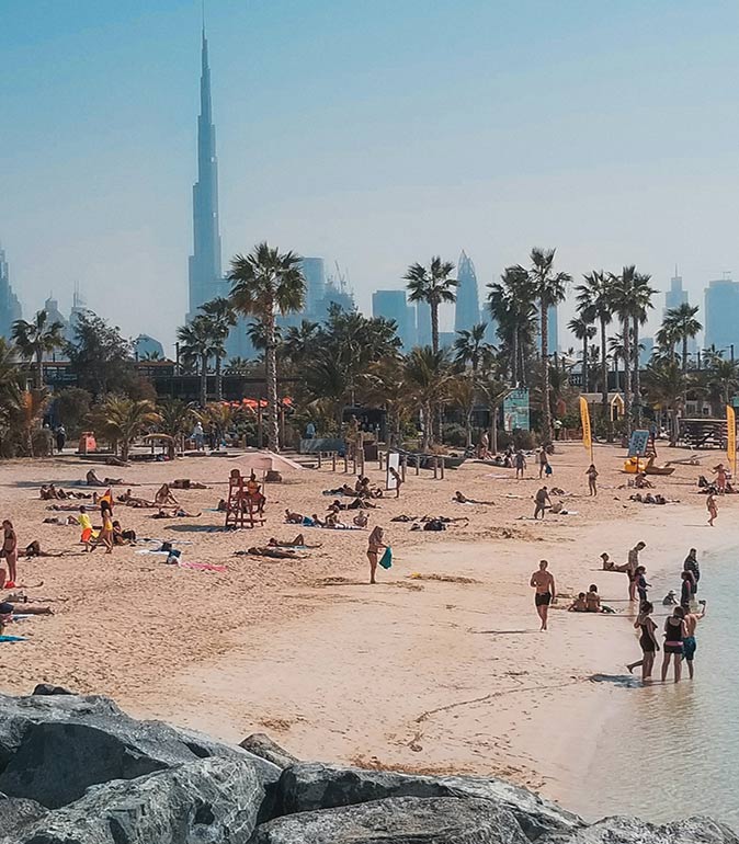 a large number of people on a sandy beach with the skyline of Dubai and palmtrees in the background