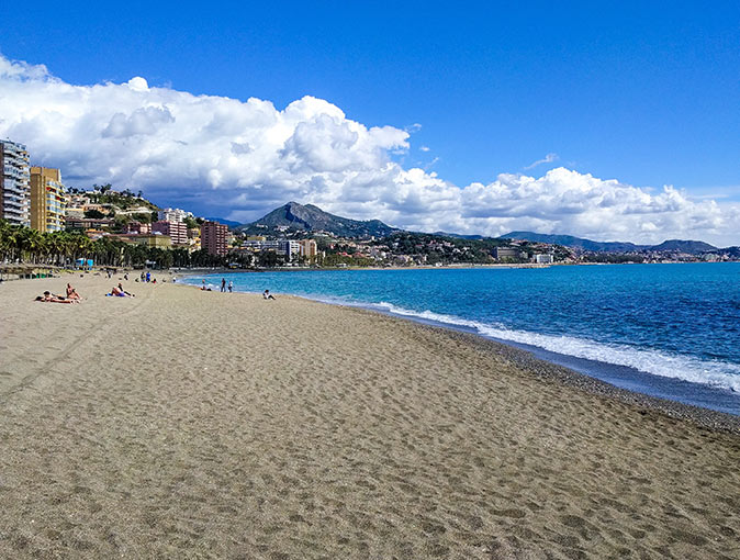 a long sandy beach with a small number of people and several buildings in the background