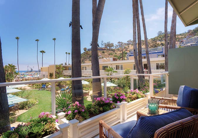 a terrace with 2 chairs looking out over a green field with palm trees