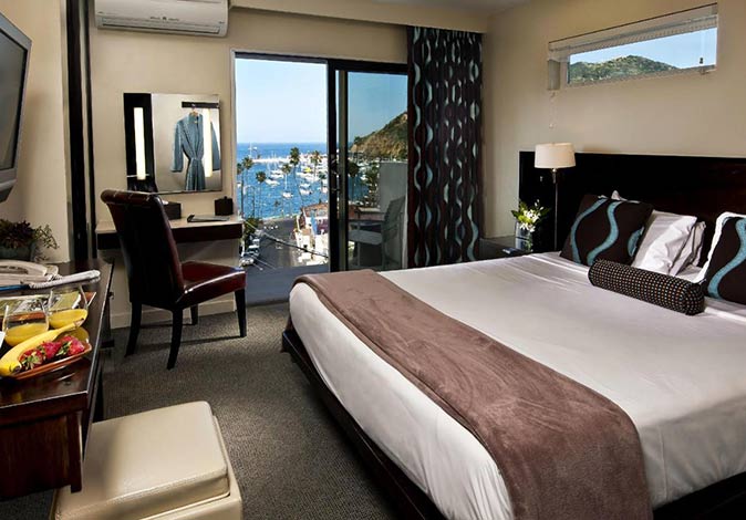 a hotel room witha large bed and a desk plus windows with a view of a bay