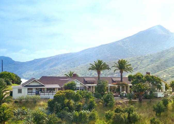 a large country house surrounded by greenery with a mountain in the background