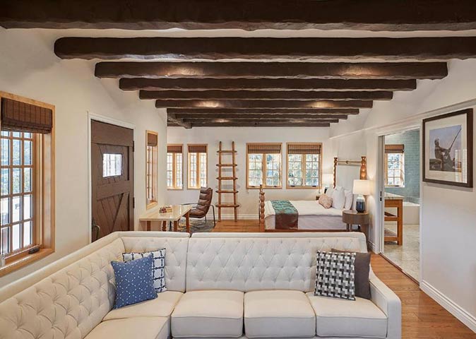 a luxury hotel room with a bed, a couch and a desk, plus wooden beams on the ceiling