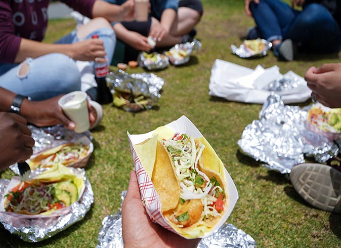 a group of people sitting on the grass eating tacos