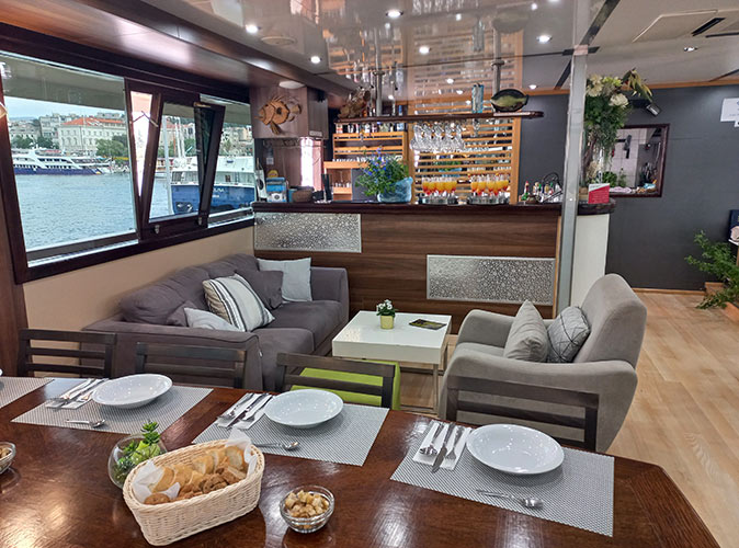 A set table in the dining area of a small ship cruise with a bar in the background