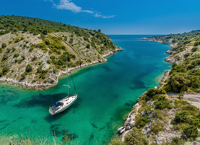 A sailing yacht anchored in blue and green water with land on both sides