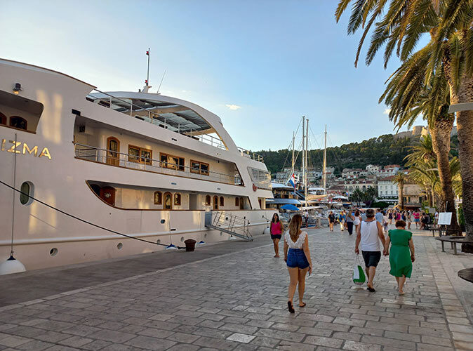 A small ship cruise docked with several people walking past it