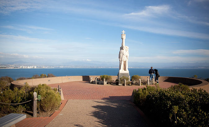 A great place to visit in San Diego on a budget A statue on a cliff with the sea and San Diego skyline in the background
