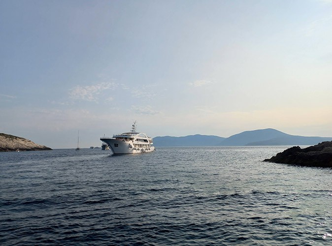 A small ship cruise at sunrise surrounded by water with some land in the distance