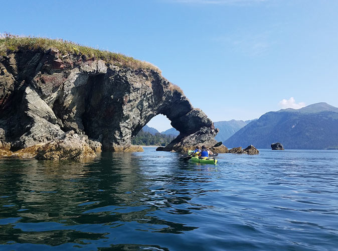 sea kayaking in Homer A kayak with 2 people in front of a rock formation