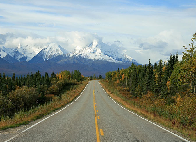 A road in Alaska with snowy mountains in the background