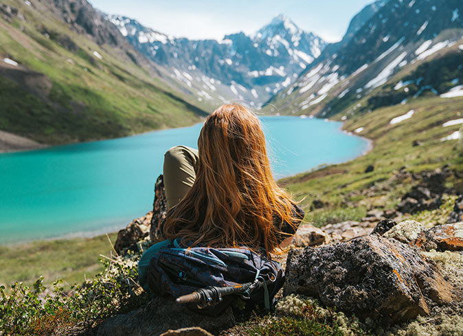 A woman sitting in the grass looking at a mountain lake