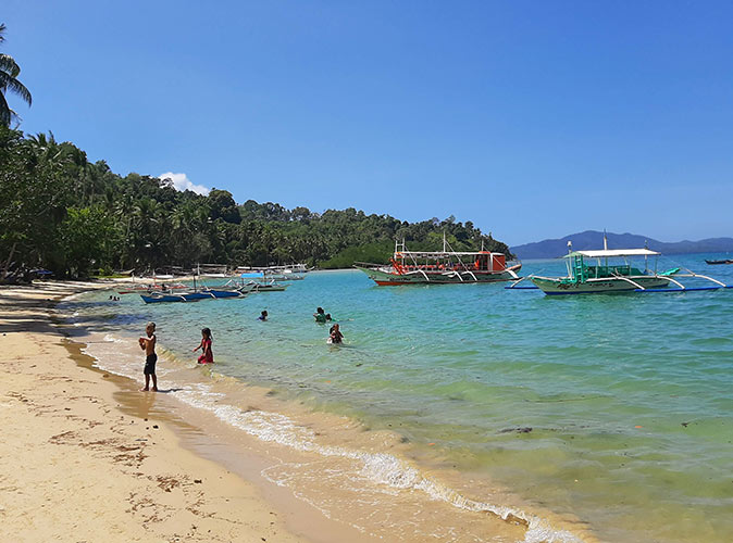 a tropical beach with several boats and kids playing