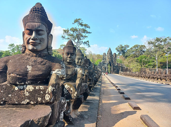 Visit Angkor Wat after your Mekong River Cruise a row of grey hindu statues next to a road