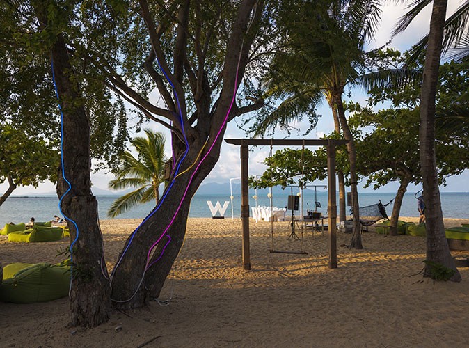trees on a sandy beach with bean bags and a swing