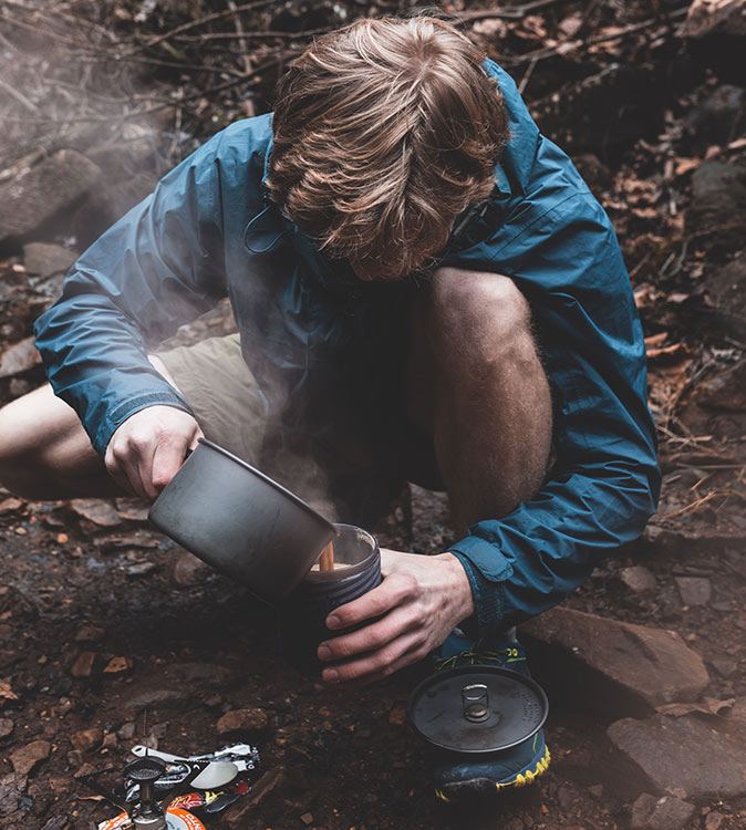 learning new skills hiking alone a man kneeling to poor some coffee from a camping stove into a cup