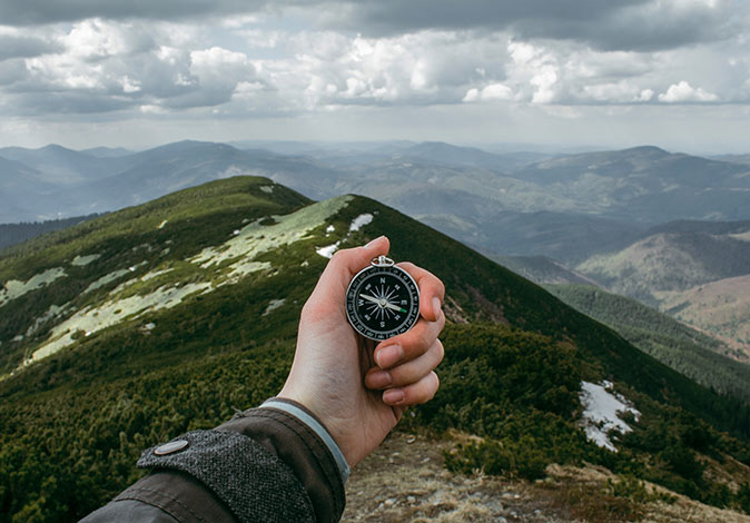 a hand holding a compass with green mountain peaks in the background