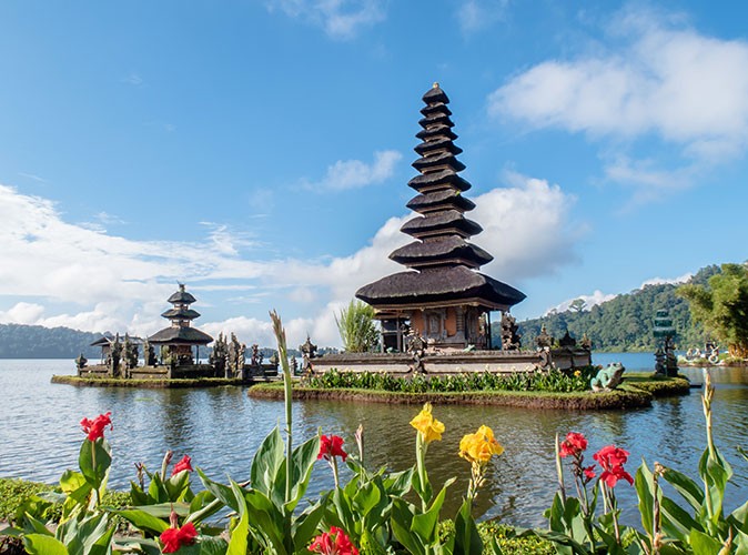 a Hindu temple surrounded by water with red and yellow flowers in the foreground
