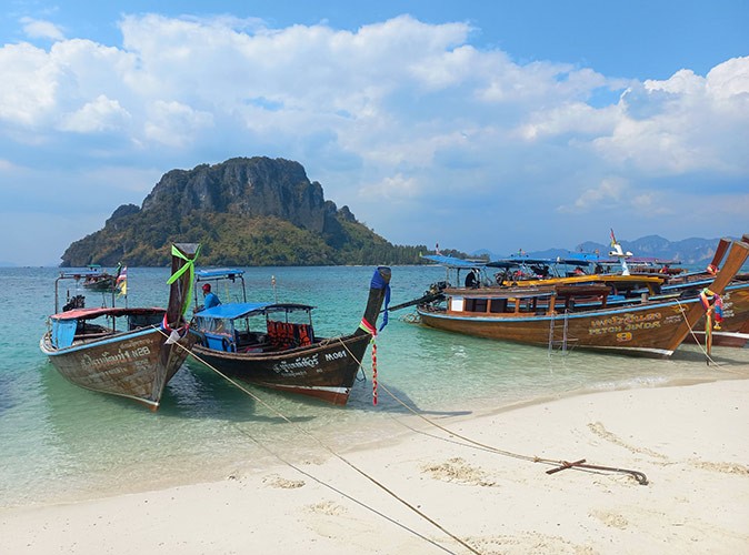 several wooden boats in front of a white sandy beach with a large rock in the background