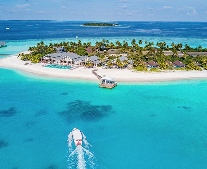 a speedboat heading towards a resort on a small island with sandy beaches and palm trees
