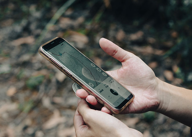A complete guide for hiking solo two hands holding a phone showing a hiking app