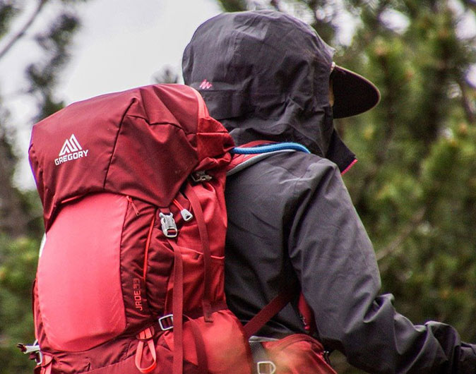 solo hiking essentials a woman photographed from behind wearing a black coat and a red hiking backpack