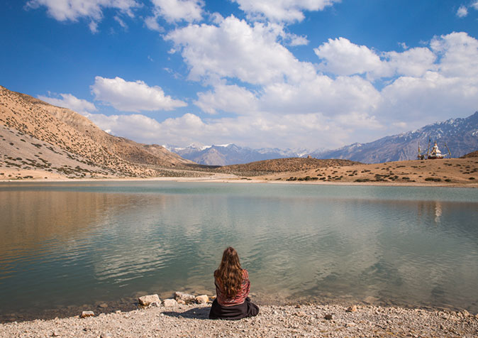 a woman sitting on a rocky beach looking out over a lake