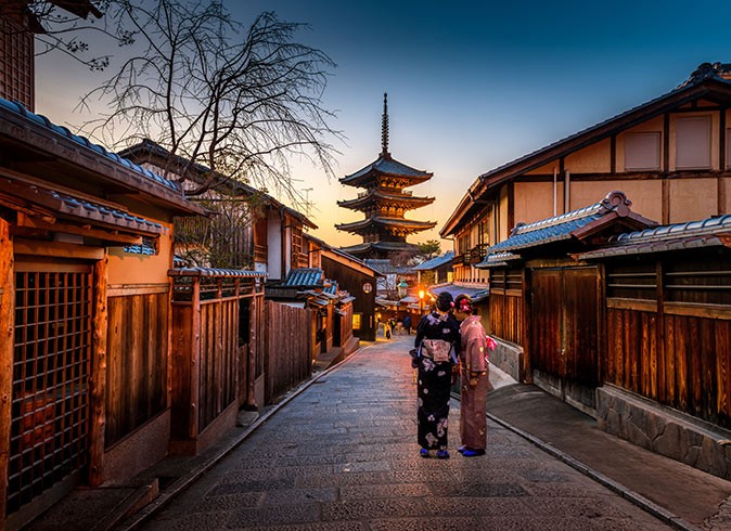 2 geisha facing away from the camera in a dark street with historic buildings