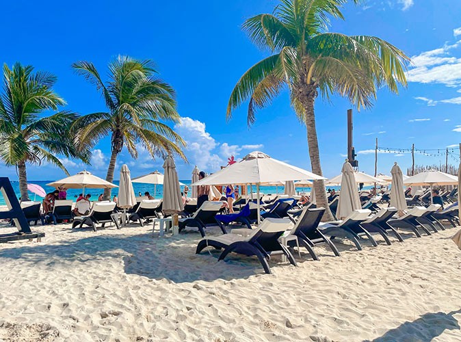 Various sun loungers and white umbrellas on a white sandy beach with palm trees