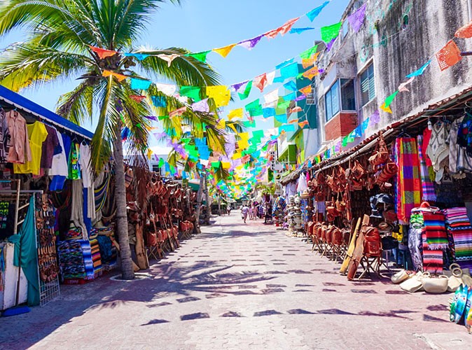 What living in Playa del Carmen is like a street lined with tourist shops, some palm trees and flags going across the street