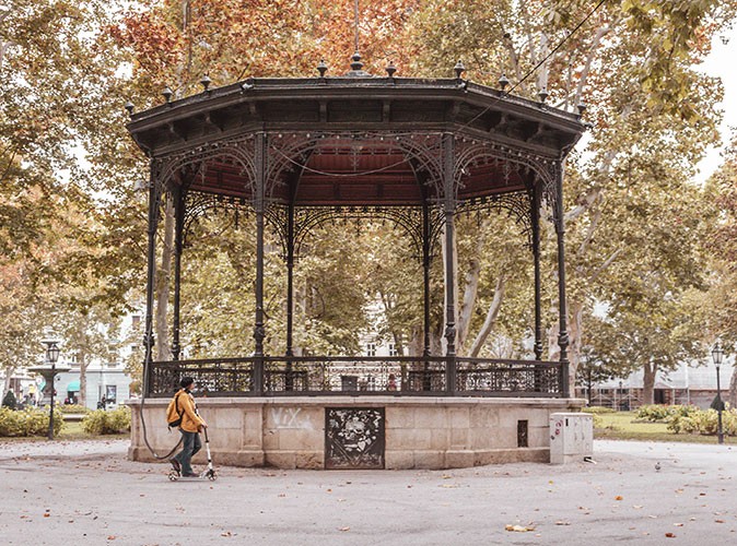 A woman on an electric scooter in front of a pergola in a park