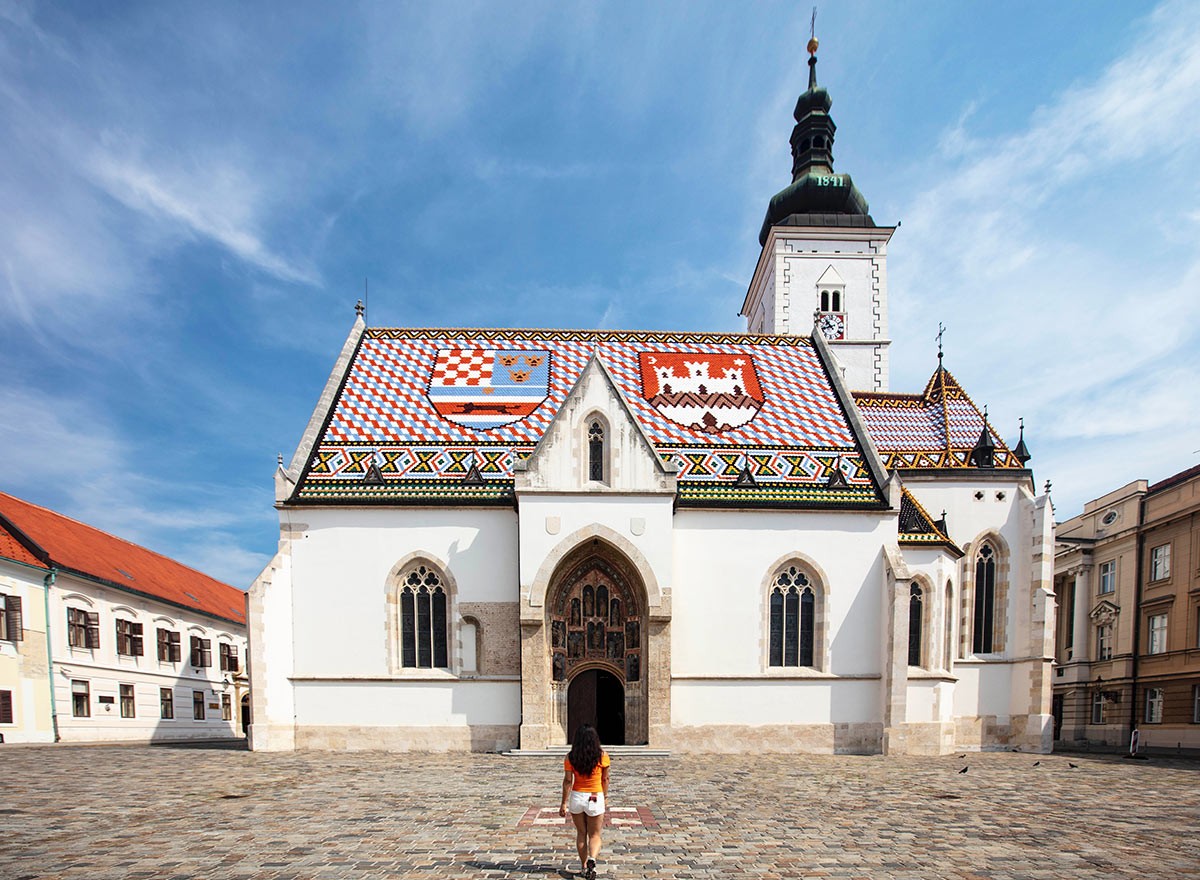 woman walking away from the camera towards a white church with a colorful roof