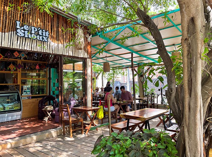 A partially covered terrace attached to a restaurant with various people sitting at wooden tables