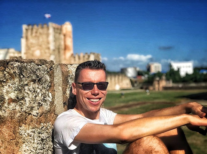 Chris living in the Dominican Republic A smiling man wearing sunglasses, leaning against a historic wall