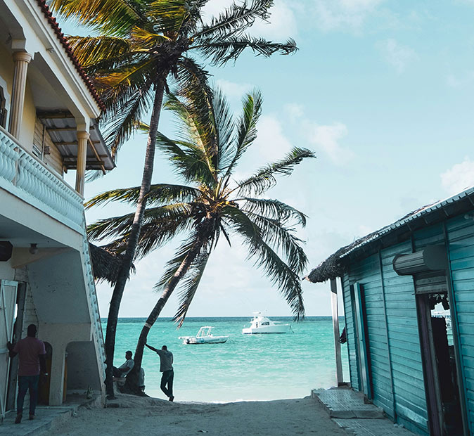 3 people standing by a beach with two buildings on the side, looking out towards 2 boats