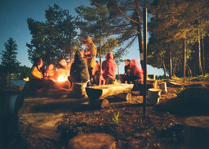 A hiking and camping tour in Canada people sitting around a campfire in a forest