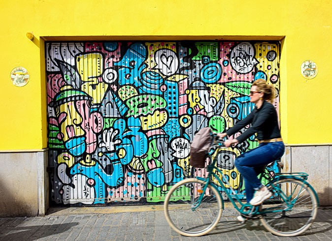 A sustainable visit to Valencia, Spain A woman on a bicycle with street art and a bright yellow wall in the background