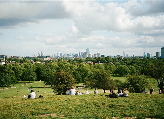 The best viewpoint to visit in Camden Town a large green park with several people and the London skyline in the background