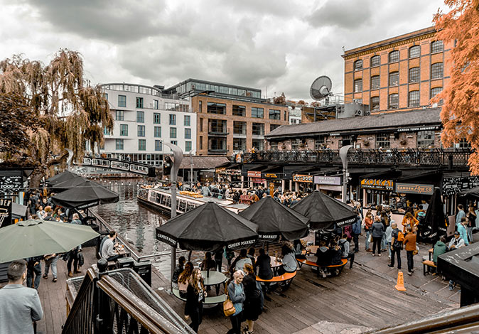 Camden Market, one of the main places to visit in Camden Town brick buildings around a canal with several shops, a terrace and a lot of people