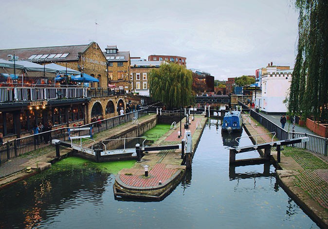 One of the main things to do in Camden Town a canal with locks, a boat and buildings on both sides