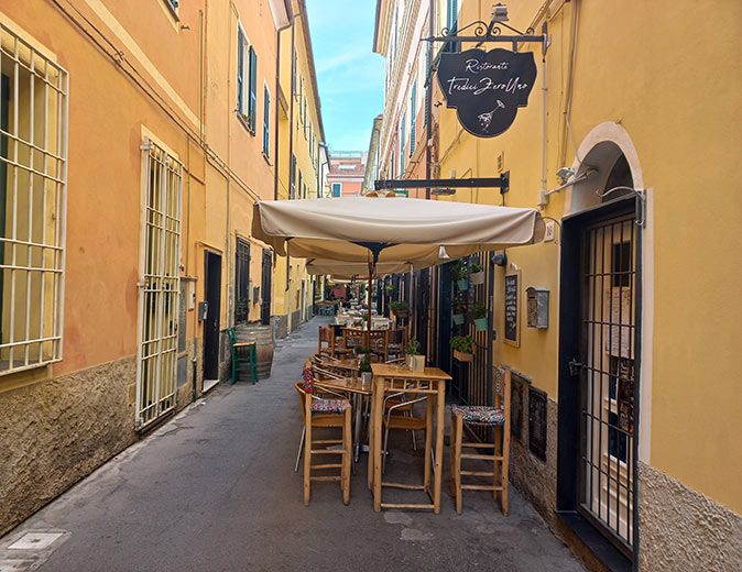 How to go off the beaten path an alley with brightly yellow painted buildings and a restaurant with tables and chairs outside