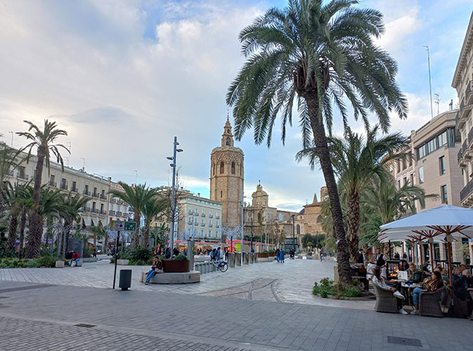 Visit Valencia sustainably by making eco-friendly choices A typical Spanish plaza with palmtrees, several people, terraces and historic buildings