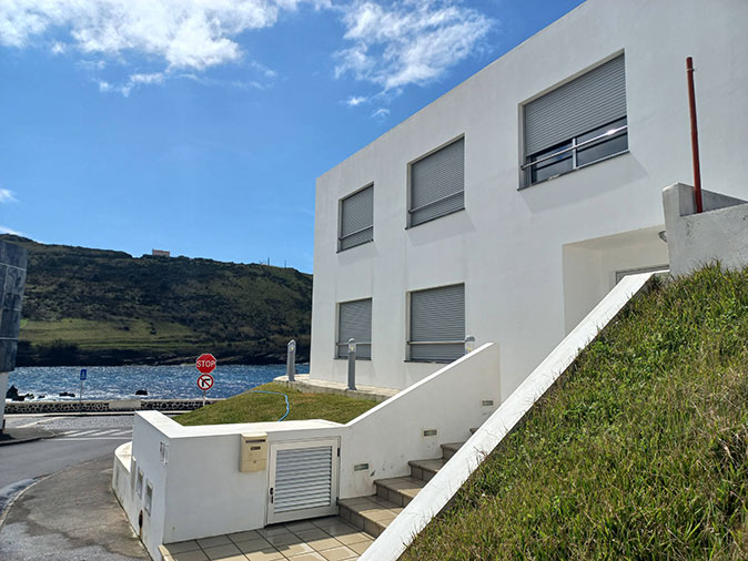 The exterior of a modern looking white building with the sea in the background