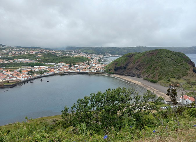 Aerial view of a bay with a beach, hills and a town in the background