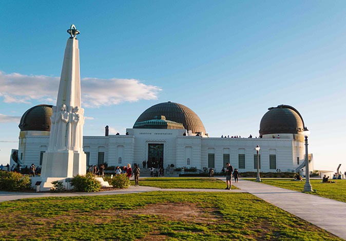 A white building with 2 domes, a green lawn and a white statue