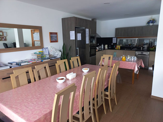 A long table with wooden chairs and a pink tablecloth with a kitchen in the background